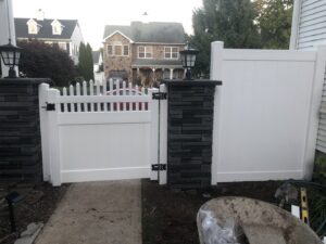 Newly installed white picket and privacy fence sections with stone pillars and outdoor lights by Mincho Contractor LLC in Jersey City, NJ