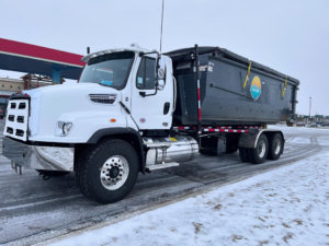 A white roll-off truck with a large dumpster on its back, ready for junk removal from First Light Services Llc in Casper, WY.