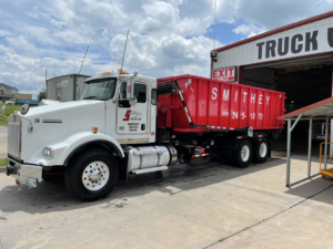 A white roll-off truck with a red dumpster, ready for junk removal services from Smithey Environmental Services LLC in Tulsa, OK.