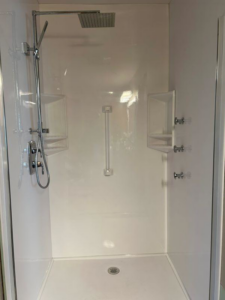 A white shower stall with modern chrome fixtures and built-in shelves by VanVleet Construction in Brooklyn Park, MN.