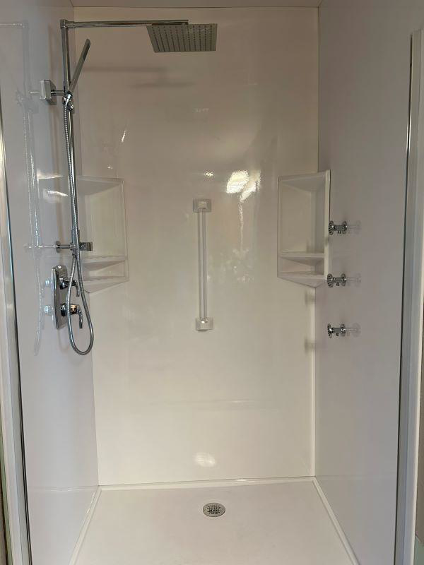 A white shower stall with modern chrome fixtures and built-in shelves by VanVleet Construction in Brooklyn Park, MN.