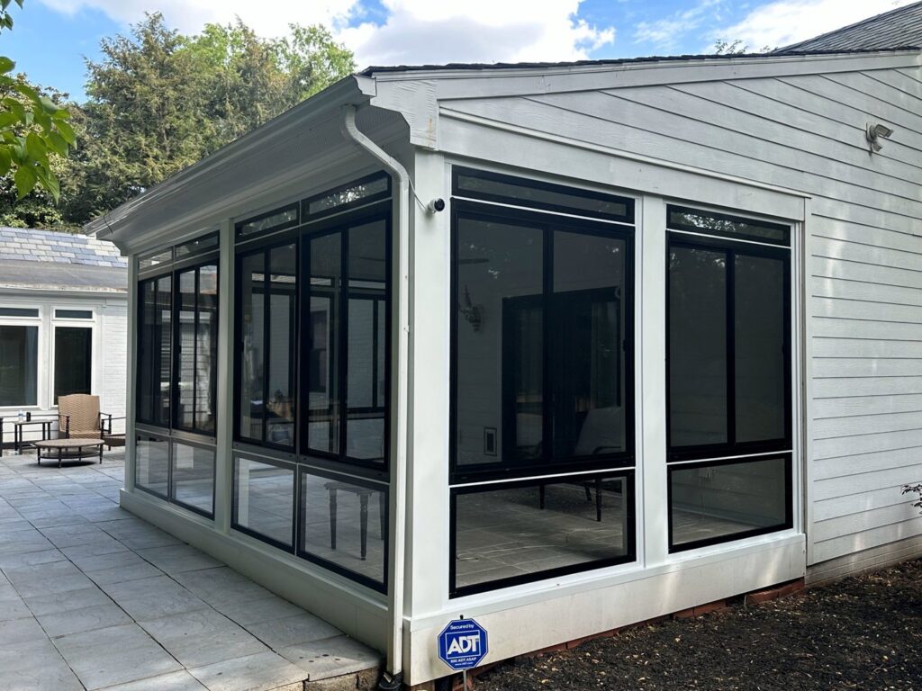 A modern sunroom addition with white siding and black window frames by X-Terior Techs in Henrico, VA.
