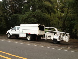 A white tree service truck with a wood chipper attached, parked by Bridgetown Tree Service in Portland, OR.