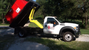 A white AA Quick Disposal truck lifting a red dumpster for junk removal service in Kansas City, MO.