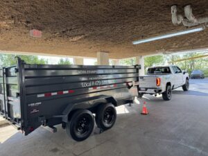 A white pickup truck towing an empty Mobiledumps dumpster trailer in Rogers, AR, for Mobiledumps Northwest Arkansas.