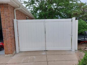 A newly installed white vinyl double gate next to a brick house, showcasing outdoor work by Jake and Jake Construction LLC in Sandy, UT.