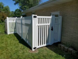 A white vinyl fence enclosure with a gate installed next to a brick house by Badger Vinyl Products in Madison, WI.