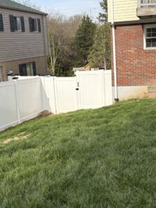 A newly installed white vinyl fence with a gate on a grassy slope by Gold-Mine Construction, LLC in Pittsburgh, PA.