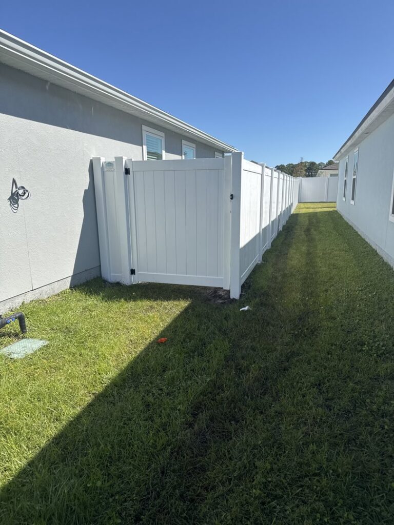 A white vinyl fence with a gate installed in a narrow side yard by NGC FENCE INC in Jacksonville, FL.