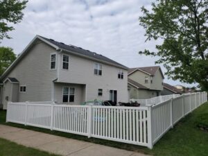 A white vinyl picket fence installed around a backyard with a house in the background by Badger Vinyl Products in Madison, WI.