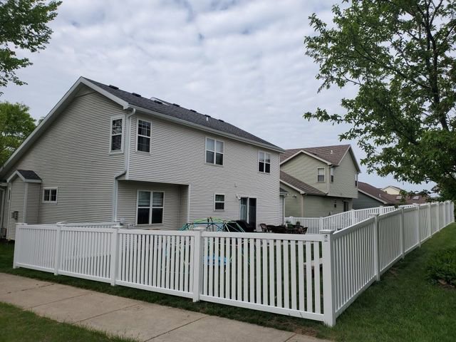 A white vinyl picket fence installed around a backyard with a house in the background by Badger Vinyl Products in Madison, WI.