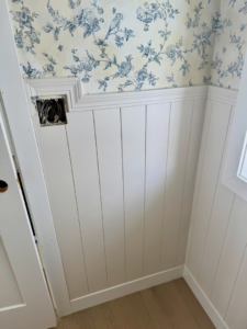 White wainscoting installed below floral wallpaper with an exposed electrical box by LIV Custom Accents in West Fargo, ND