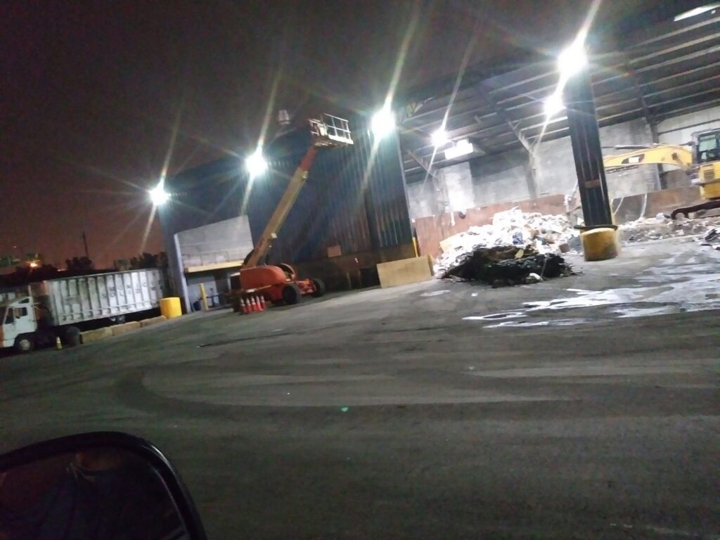 A wide view of a junk processing facility showing large piles of waste and an excavator, managed by Lemcor in Newark, NJ.