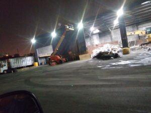 A wide view of a junk processing facility showing large piles of waste and an excavator, managed by Lemcor in Newark, NJ.