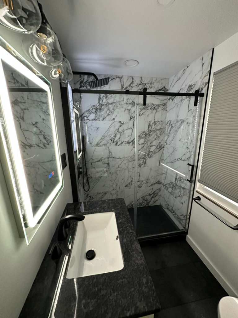 A wide view of a modern bathroom renovation with vanity, illuminated mirror, and glass shower by Tap & Tile Inc. in East Pittsburgh, PA.