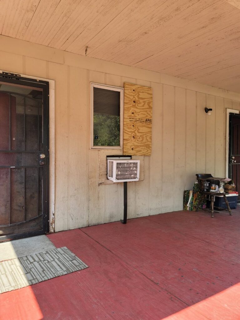 Exterior view showing a window AC unit and a boarded-up window, indicating repair work by Friendly Handyman LLC in Wichita, KS