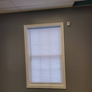 A window with new white horizontal blinds installed on a grey wall, a handyman service provided by Reshaud Renovation LLC in Richmond, VA.
