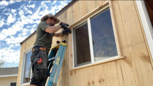 A handyman installing a window or exterior trim on a wooden building by Top Shelf Handyman Pros in Post Falls, ID