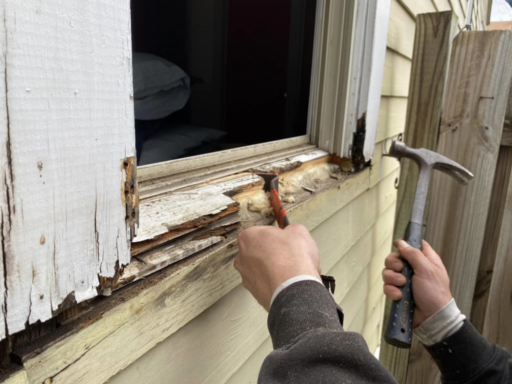 Hands repairing rotten wood around an exterior window frame, a service provided by Atlanta Handyman and Repair LLC in Johns Creek, GA.