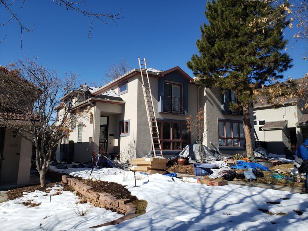 A residential roofing project in progress during winter, with ladders and tarps, by Jesse Roofs Co. in Denver, CO