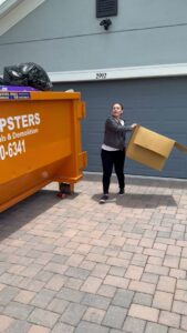 A woman loading a large cardboard box into an orange dumpster from Pro Dumpsters & Junk Removal in Orlando, FL.