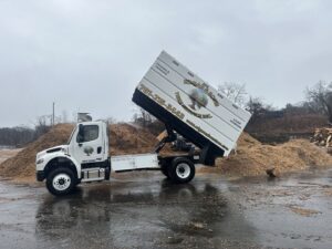 A dump truck from Edgar&son's landscaping unloading wood chips after a tree service job in Boston, MA