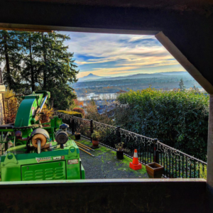 A green wood chipper at a Triple Acorn Tree Service job site in Portland, OR, with a scenic view of the city.