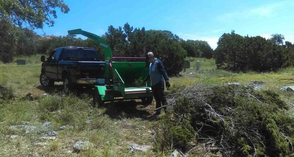 A wood chipper processing tree branches, with a worker nearby, demonstrating debris removal by Lone Star Tree Service & Landscaping in Fort Worth, TX.