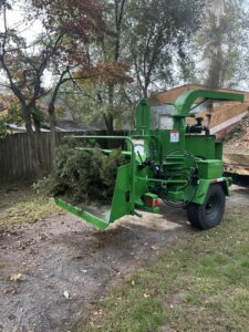 A wood chipper processing tree debris and logs on the ground after a tree service job by Gibbs Tree Service in Seaford, DE.