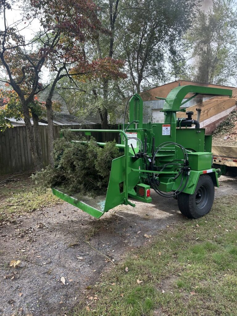 A wood chipper processing tree debris and logs on the ground after a tree service job by Gibbs Tree Service in Seaford, DE.