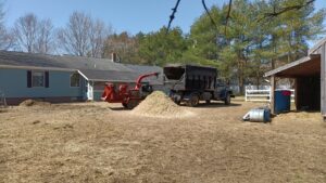 A wood chipper, dump truck, and a pile of wood chips after a tree service job by Maine Tree Guy LLC in Auburn, ME.