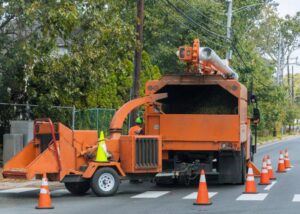 A large orange wood chipper truck processing tree debris on a street, used by Rhode Island Tree Removal in Providence, RI.