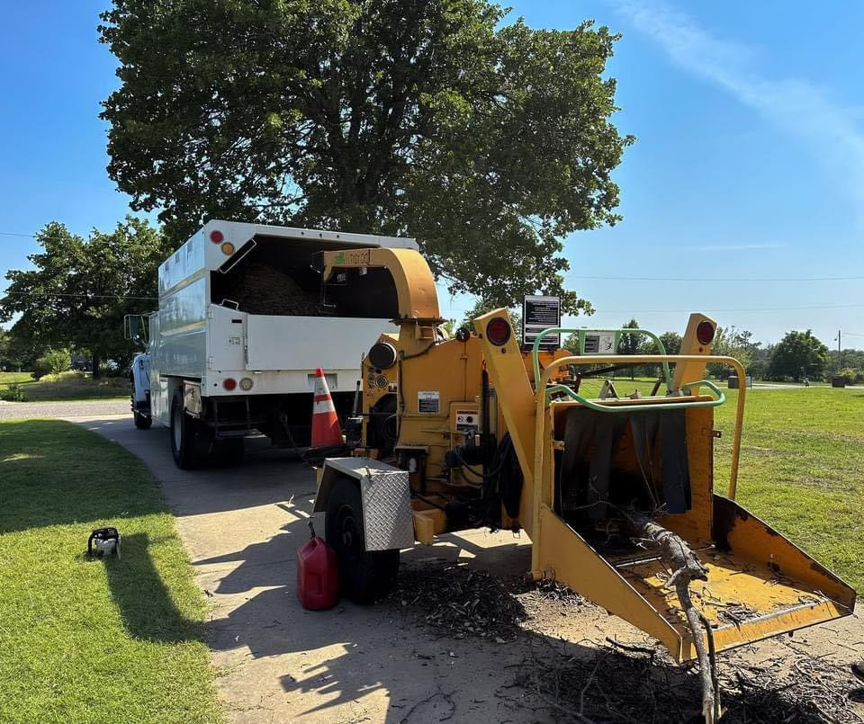 A wood chipper and dump truck processing tree branches for Firestorm Tree Specialists in Oklahoma City, OK.