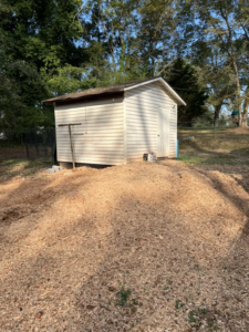 A large mound of wood chips from a recent stump removal project next to a backyard shed by Manley's Stump Grinding in Opelika, AL.