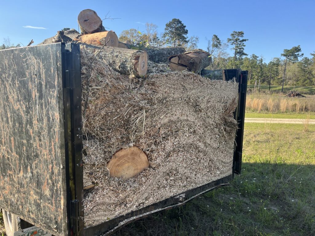 A dump trailer filled with wood chips and logs, ready for disposal by Solid Ground Tree & Property Services LLC in Dothan, AL.