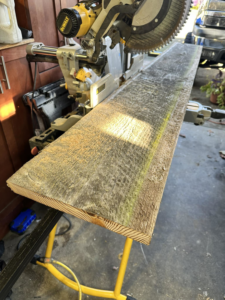 A wooden board positioned next to a miter saw, being prepared for cutting for a custom project by Valleys Finest Custom Finishes LLC in Salem, OR.