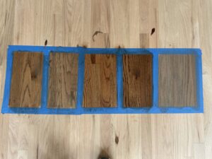 Various wood floor stain samples taped to a light hardwood floor for selection by Glenni Floors LLC in Roswell, GA.