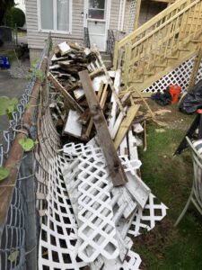 A large pile of wood and lattice debris next to a fence and outdoor stairs, ready for removal by Rizzo Junk Removal in Nashua, NH.
