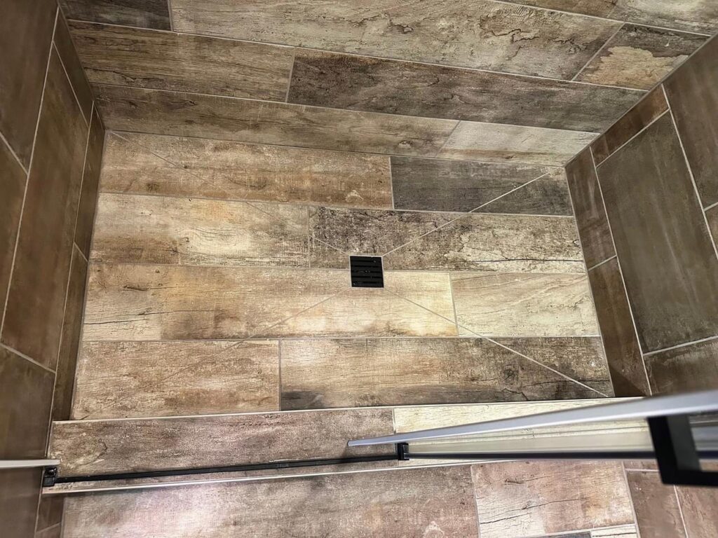 Close-up view of a wood-look tile shower floor with a modern drain, installed by Supreme Tile & Flooring in Charlotte, NC.
