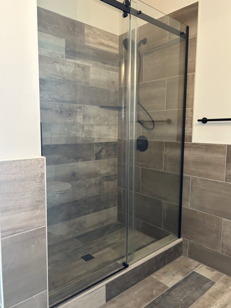 Modern shower with wood-look tiles on the walls and floor, enclosed by a glass door, installed by Supreme Tile & Flooring in Charlotte, NC.