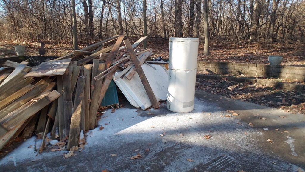 A pile of wood and an old tank or water heater outdoors, indicating a junk removal job by Kaveman Hauling LLC in Ankeny, IA.
