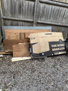 A pile of wood planks and a cardboard box for an outdoor deck box, ready for debris removal by Junk Removal Brothers in Worcester, MA.