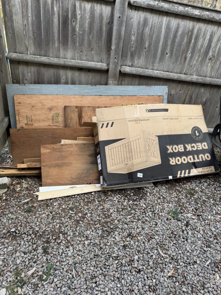 A pile of wood planks and a cardboard box for an outdoor deck box, ready for debris removal by Junk Removal Brothers in Worcester, MA.