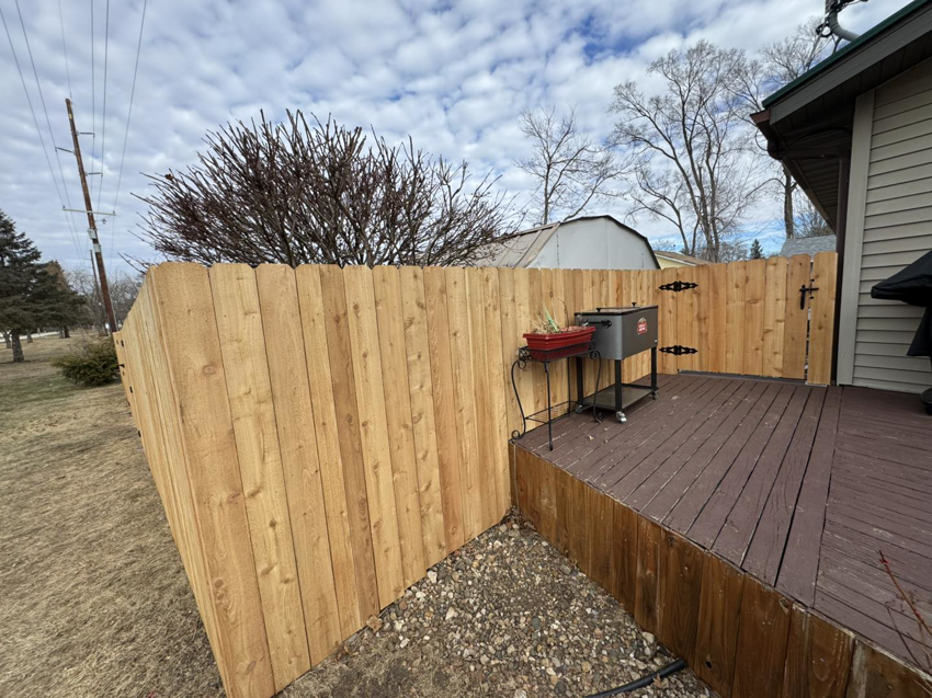 A wooden privacy fence with a gate installed adjacent to a residential deck by Bergmann Fencing Co. in Cedar Falls, IA.