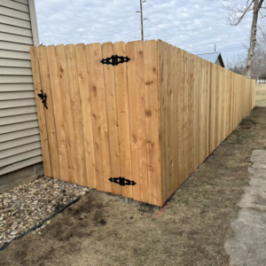 A corner section of a wooden privacy fence featuring decorative black hinges and a latch, installed by Bergmann Fencing Co. in Cedar Falls, IA.