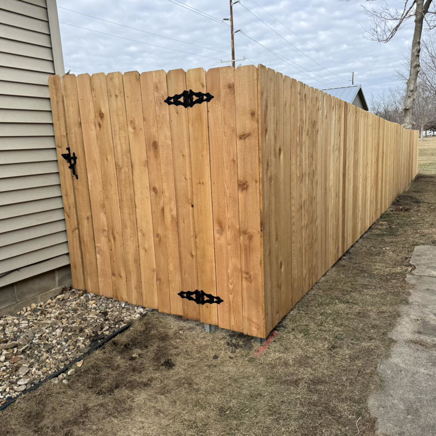A corner section of a wooden privacy fence featuring decorative black hinges and a latch, installed by Bergmann Fencing Co. in Cedar Falls, IA.