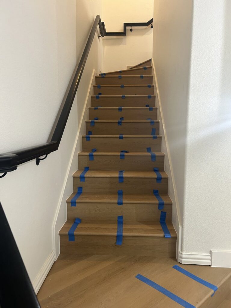 Wood stair tread installation in progress, protected by blue tape, by MDN Roofing 2 Flooring LLC in Fort Worth, TX.