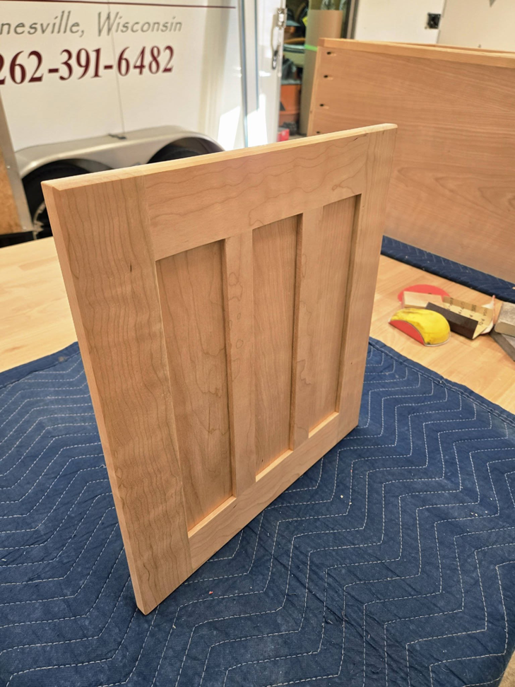 A newly crafted wooden cabinet door or panel on a padded surface by Kingsbury Builders LLC in Janesville, WI