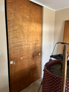 A wooden closet door being prepped for repair or painting, with a ladder nearby, by Lambert's Residential Painting And More LLC in Fort Wayne, IN.