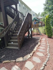 Wooden deck stairs leading to a stone path and mulched area, installed by Mels Haul & Junk Removal in Raleigh, NC.
